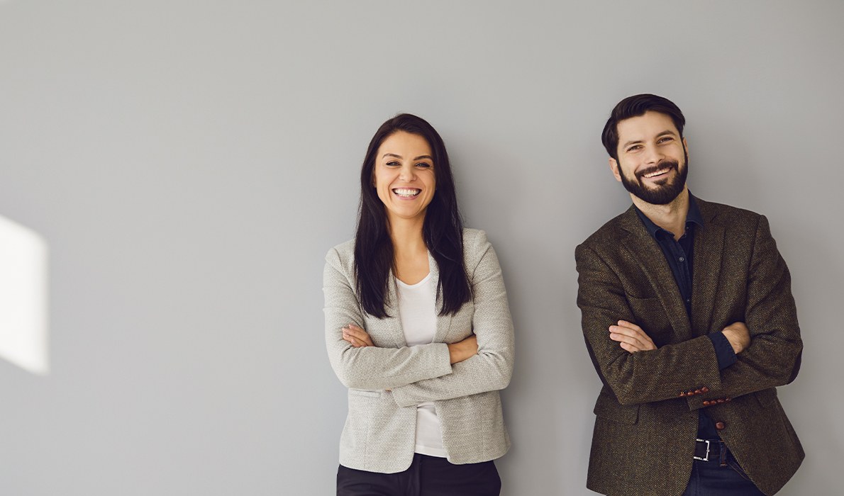 Man and woman in business attire smiling against white wall