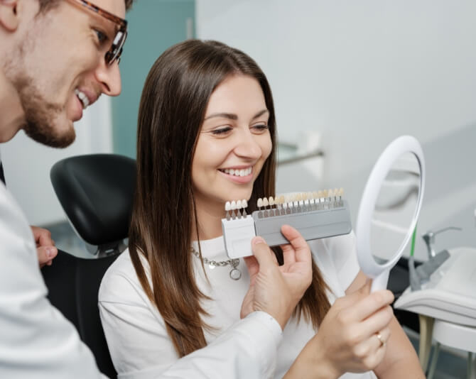 Cosmetic dentist helping smiling patient pick shade of veneer