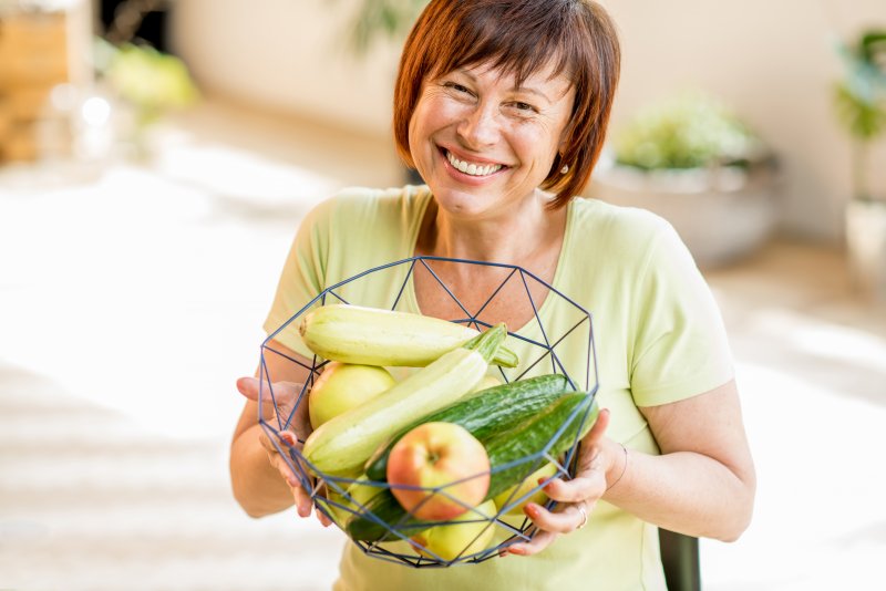 a middle-aged woman holding a basket of vegetables and fruit while wearing dental implants in Edison