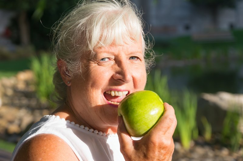 older woman with dentures eating apple outside during summer