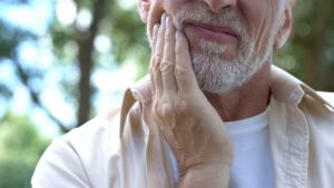 patient holding his face with dental implant failure