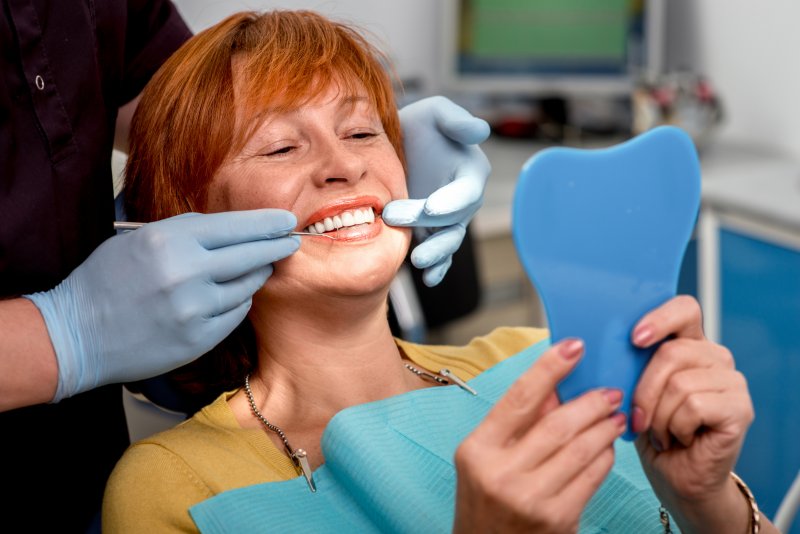 A senior woman admiring her dental implants in a hand mirror