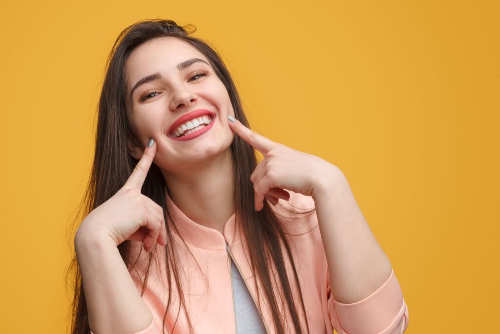 Woman pointing to her smile with two fingers with yellow background